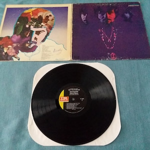 May include: A vinyl record album cover with a purple and black design. The front cover features a collage of faces with a purple background. The back cover features a single face with a purple background. The album title is "Badfinger" and the record label is "Apple Records".