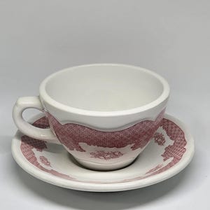 May include: White teacup and saucer set with a red floral pattern. The teacup has a handle and sits on a matching saucer. The design is a classic style, suitable for serving tea or coffee.
