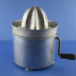 May include: A vintage silver-colored manual citrus juicer with a reamer and a handle. The juicer has a round base and a removable top.