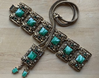 May include: A gold tone bracelet with a chain and a series of green and white stone embellishments.