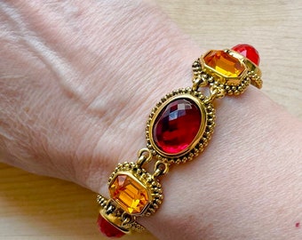 May include: Gold bracelet with red and orange faceted gemstones. The bracelet has a beaded design.