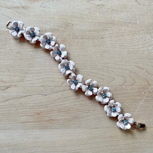 Op de afbeelding: Een delicate armband met een ketting van lichtroze bloembedels met blauwe strass steentjes in het midden.