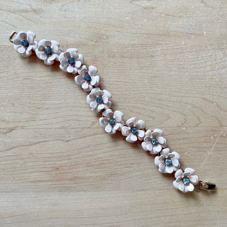 Op de afbeelding: Een delicate armband met een ketting van lichtroze bloembedels met blauwe strass steentjes in het midden.