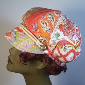May include: A colourful patchwork fabric hat with a floral design and a white rope accent. The hat is quilted and has a button on the side.