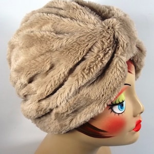 May include: A brown faux fur turban hat. The hat is made of soft, plush fabric and has a knotted design.