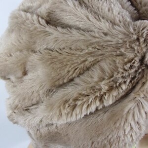 May include: A close-up of a light brown faux fur fabric. The fabric has a soft, fluffy texture and is ideal for crafting projects.