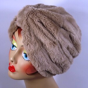 May include: A brown faux fur turban hat. The hat is made of soft, plush fabric and has a gathered, draped design.