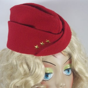 May include: A red felt hat with a folded brim and four gold stars. The hat is worn on a mannequin with blonde hair.
