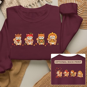 May include: A maroon long-sleeve sweatshirt featuring a graphic of four cartoon squirrels wearing sweaters and hats, each holding autumn-themed items. A smaller inset shows the same graphic with the text OPTIONAL BACK PRINT.