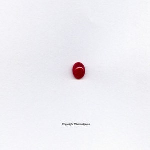 May include: A single, round, red gemstone cabochon on a white background.