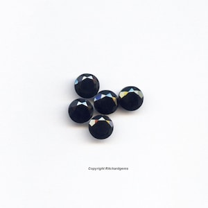 May include: Five black round gemstones with a faceted cut. The gemstones are arranged in a cluster on a white background.
