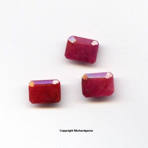 Könnte beinhalten: Drei rote Edelstein-Cabochons mit facettiertem Schliff. Die Edelsteine sind rechteckig und haben eine leicht irisierende Oberfläche.