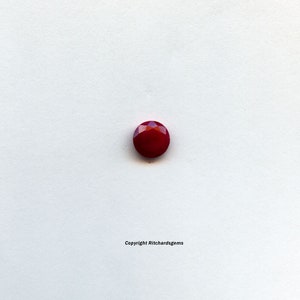 May include: A deep red gemstone with a faceted cut. The gemstone is round and has a high polish.