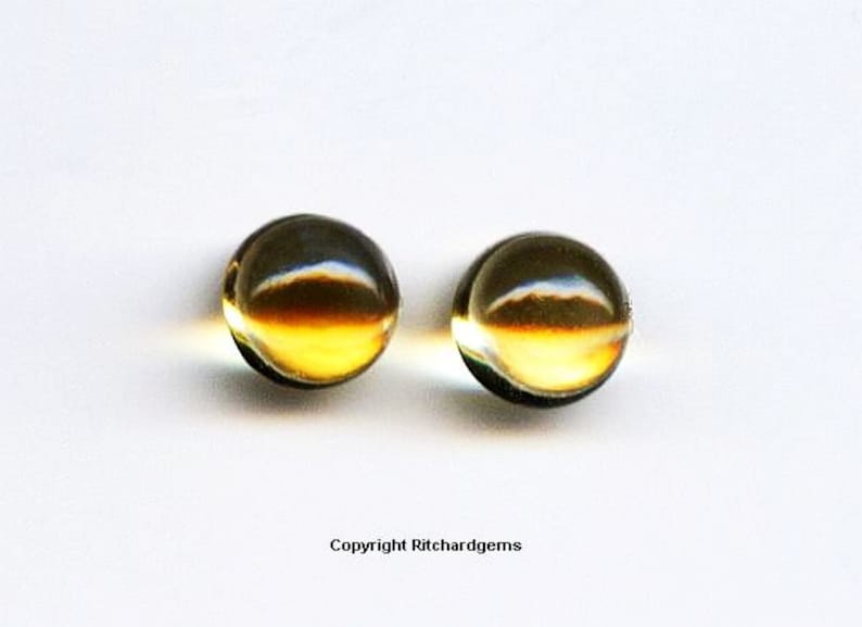 May include: Two round, clear glass beads with a golden yellow hue. The beads are smooth and have a slight shimmer.