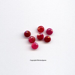 May include: Seven red gemstone beads with faceted surfaces. The beads are arranged in a loose cluster on a white background.