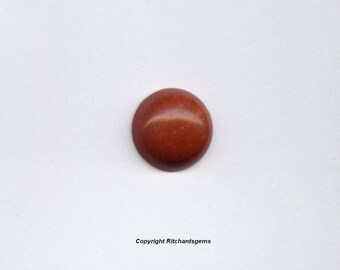 May include: A round, red cabochon gemstone with a smooth, polished surface.