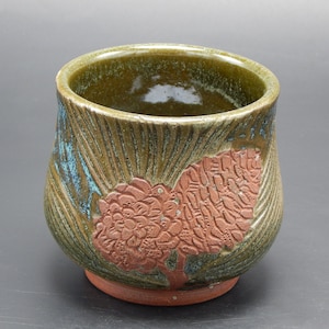 Może przedstawiać: Zielony kubek ceramiczny z brązowym wzorem szyszki. Kubek ma fakturowaną powierzchnię i szeroki rant.