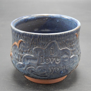 Könnte beinhalten: Eine blaue Keramikschüssel mit einer strukturierten Oberfläche und einem erhabenen Design aus Wolken und Vögeln. Die Schüssel trägt die Inschrift "I love you" an der Seite.