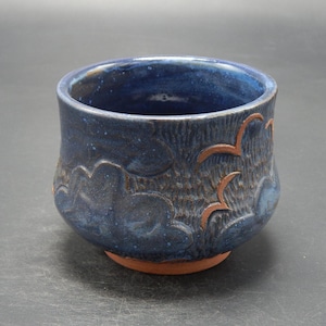 Könnte beinhalten: Eine kleine, dunkelblaue Keramikschale mit einer strukturierten Oberfläche und einem Design aus stilisierten Wolken. Die Schale hat einen leicht ausgestellten Rand und einen abgerundeten Boden.