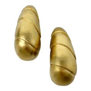 May include: A pair of gold-toned earrings with a textured, ribbed design. The earrings are shaped like teardrops.