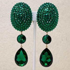 May include: A pair of emerald green statement earrings. Each earring features a large, round, textured top, a smaller circular gem, and a teardrop-shaped gem. The earrings are suspended from gold-colored findings.