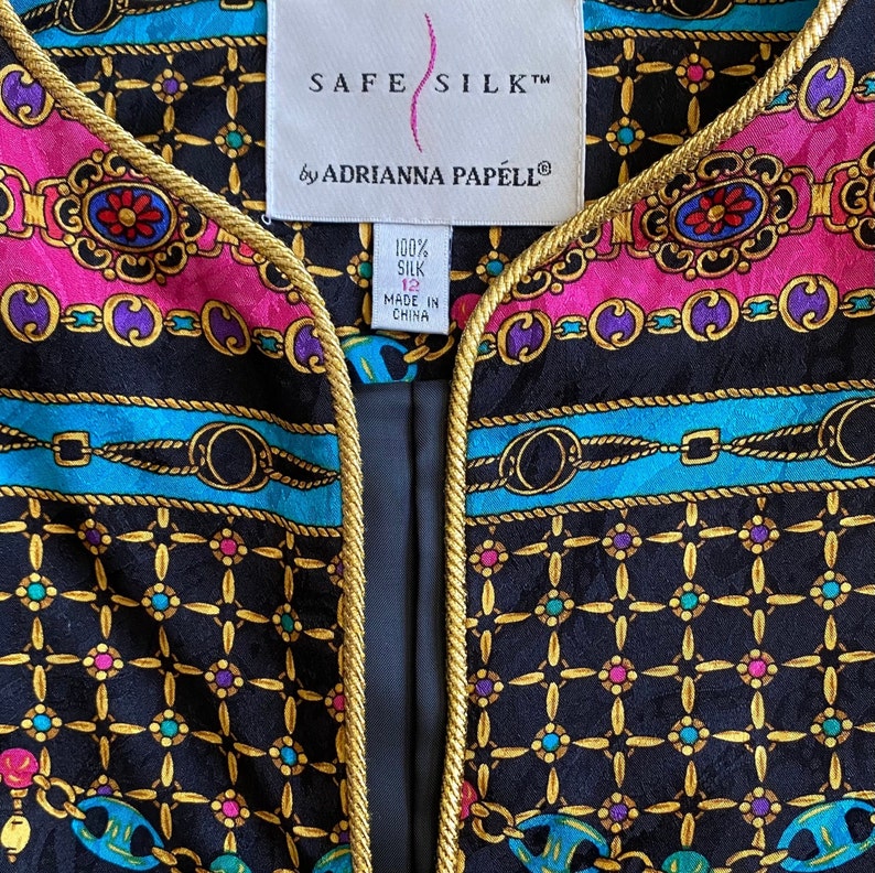 May include: A black silk jacket with gold trim and a colorful chain print. The label reads "SAFE SILK&trade; by ADRIANNA PAPELL&reg; 100% SILK 12 MADE IN CHINA".