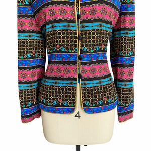May include: A black blazer with a colorful patterned design featuring chains, geometric shapes, and floral motifs. The blazer has a gold trim and a button closure.