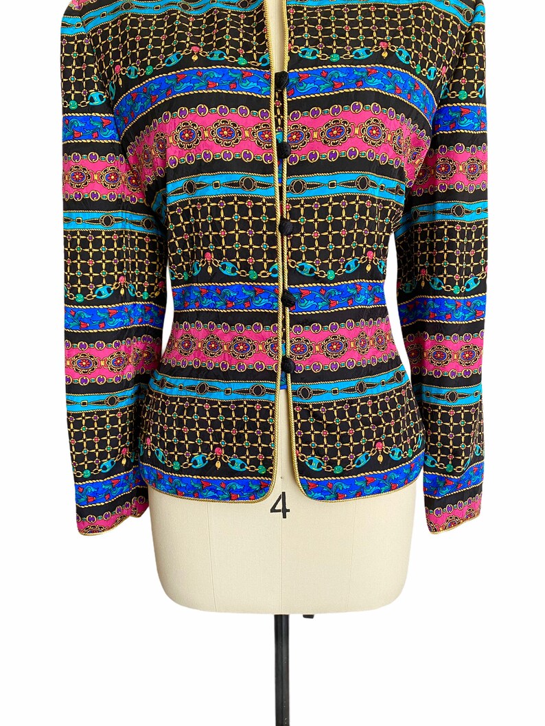 May include: A black blazer with a colorful patterned design featuring chains, geometric shapes, and floral motifs. The blazer has a gold trim and a button closure.