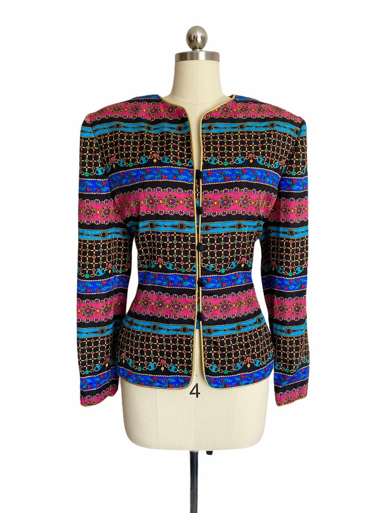 May include: A black blazer with a colorful geometric pattern featuring pink, blue, and gold accents. The blazer has a gold trim and a single button closure.