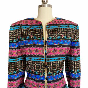 May include: A black, long-sleeved jacket with a gold trim and a colorful geometric pattern. The pattern features blue, pink, and green stripes with gold chains and other decorative elements.