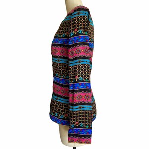 May include: A black, long-sleeved jacket with a colorful geometric pattern. The pattern features pink, blue, and gold accents. The jacket has a button closure and a fitted silhouette.