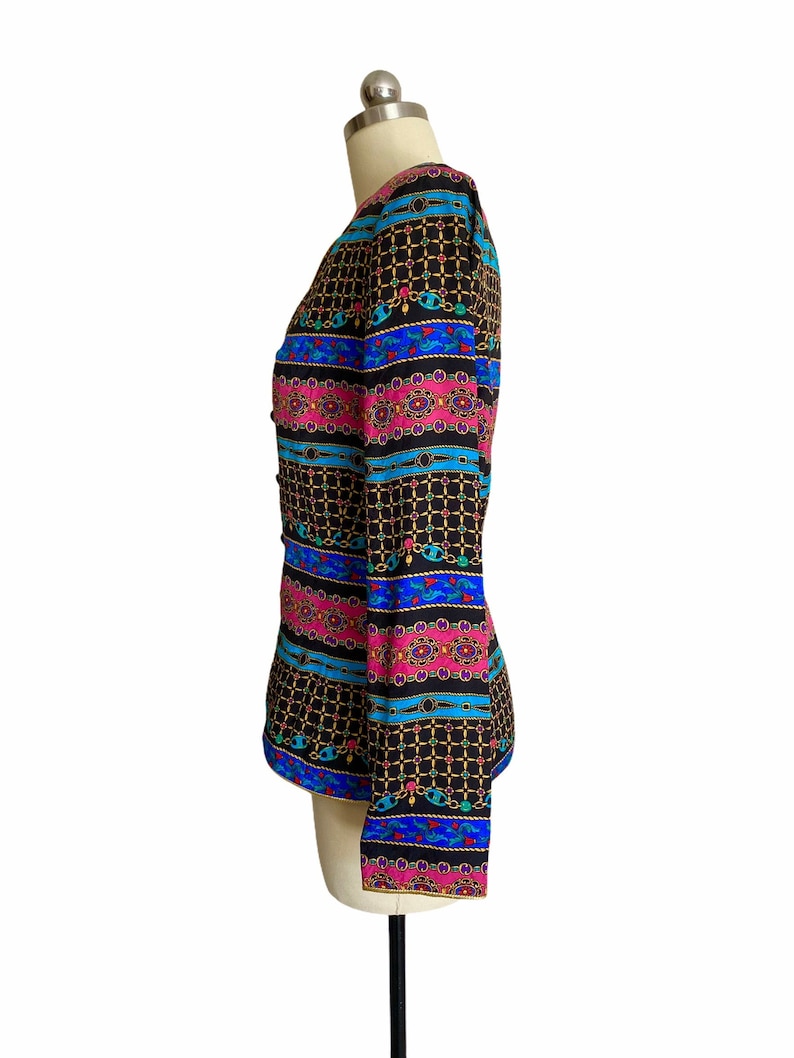 May include: A black, long-sleeved jacket with a colorful geometric pattern. The pattern features pink, blue, and gold accents. The jacket has a button closure and a fitted silhouette.