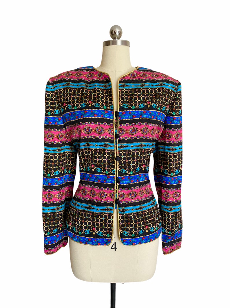 May include: A black blazer with a colorful patterned design featuring gold chains, pink, blue, and green accents. The blazer has a gold trim and a single button closure.