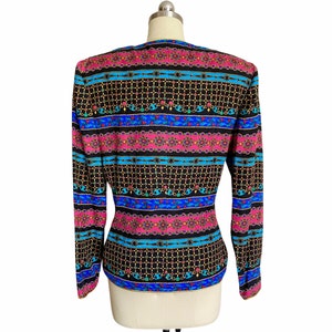 May include: A black long-sleeved blouse with a colorful geometric pattern featuring pink, blue, and gold accents. The pattern is reminiscent of a chain link design.