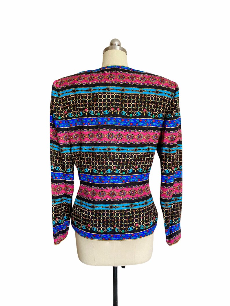 May include: A black long-sleeved blouse with a colorful geometric pattern featuring pink, blue, and gold accents. The pattern is reminiscent of a chain link design.