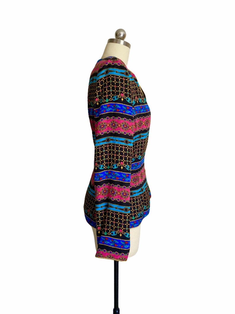 May include: A black, long-sleeved blouse with a colorful geometric pattern featuring pink, blue, and gold accents. The pattern is reminiscent of a chain link design.