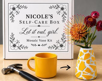 May include: A white rectangular box labeled Nicole's Self-Care Box Let it out, girl. Mosaic Vase Kit with floral borders, a yellow ceramic mug, a metal hammer with a black handle, and a yellow and white mosaic vase holding orange and red flowers.