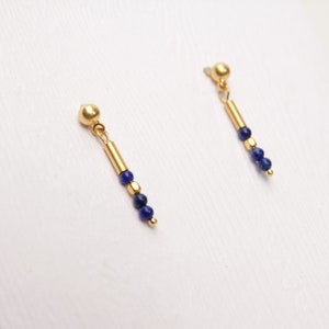 Peut inclure: Une paire de boucles d'oreilles en or avec une perle de pierre précieuse bleue suspendue et une barre en or.