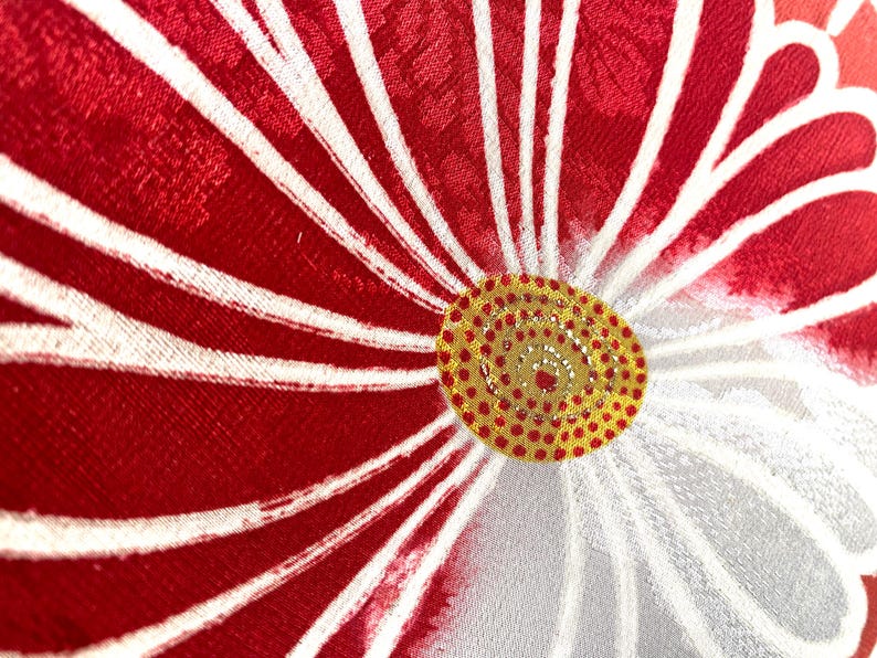 May include: Close-up of a floral design with red petals and white stripes radiating from a yellow and red center. The fabric has a textured appearance, with a detailed pattern.