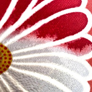 May include: Close-up of a floral design with a red and white petal pattern. The center of the flower is yellow with red dots. The design is on a round, red background.