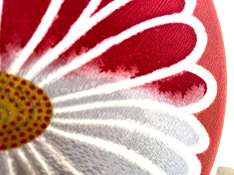 May include: Close-up of a floral design with a red and white petal pattern. The center of the flower is yellow with red dots. The design is on a round, red background.