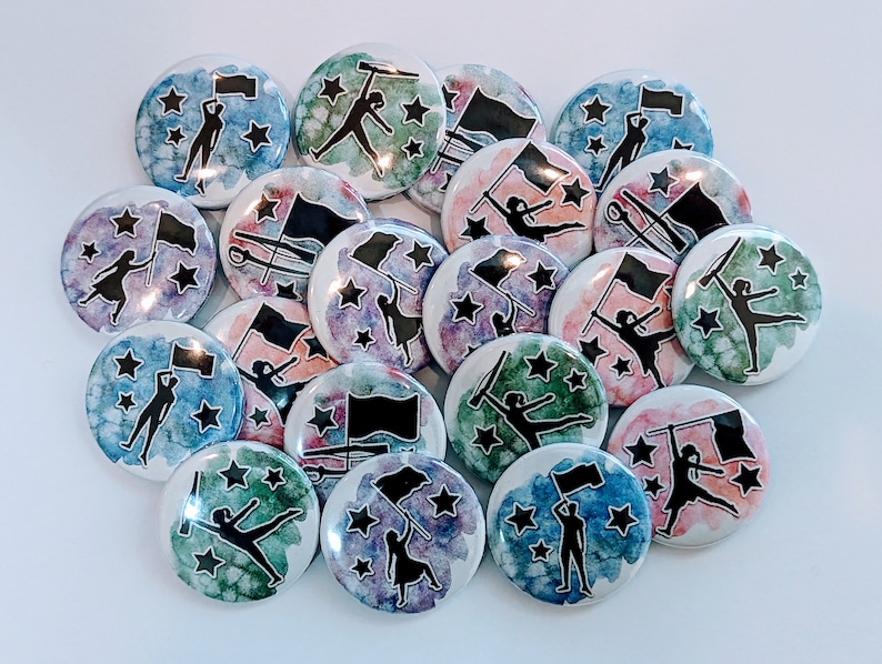 May include: A collection of 17 watercolor painted pinback buttons featuring silhouettes of color guard members with flags and stars. The buttons are in various shades of blue, green, pink, and purple.