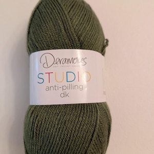 May include: A ball of olive green yarn with a white label. The label reads "Deramores STUDIO anti-pilling dk" in a colorful font. The yarn is tightly wound and appears soft, suitable for knitting and crochet projects.