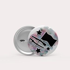 May include: A white button with a watercolor background in shades of pink, blue, and green. The button features a black silhouette of a color guard flag, two rifles crossed, and three stars.
