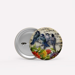 May include: A vintage-style button featuring three blue birds perched on a branch with flowers. The background is a faded, cream-colored paper with text in a foreign language.