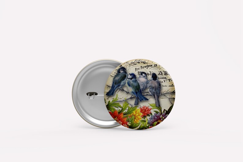 May include: A vintage-style button featuring three blue birds perched on a branch with flowers. The background is a faded, cream-colored paper with text in a foreign language.
