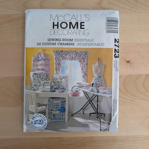May include: A McCall's Home Decorating sewing pattern envelope, number 2723, featuring illustrations of sewing room essentials including a hanging organizer, machine covers, curtains, a dress form, and an ironing board with a floral fabric print.