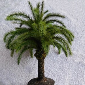 May include: A small artificial palm tree with green fronds and a brown trunk. The tree is potted in a dark brown pot.