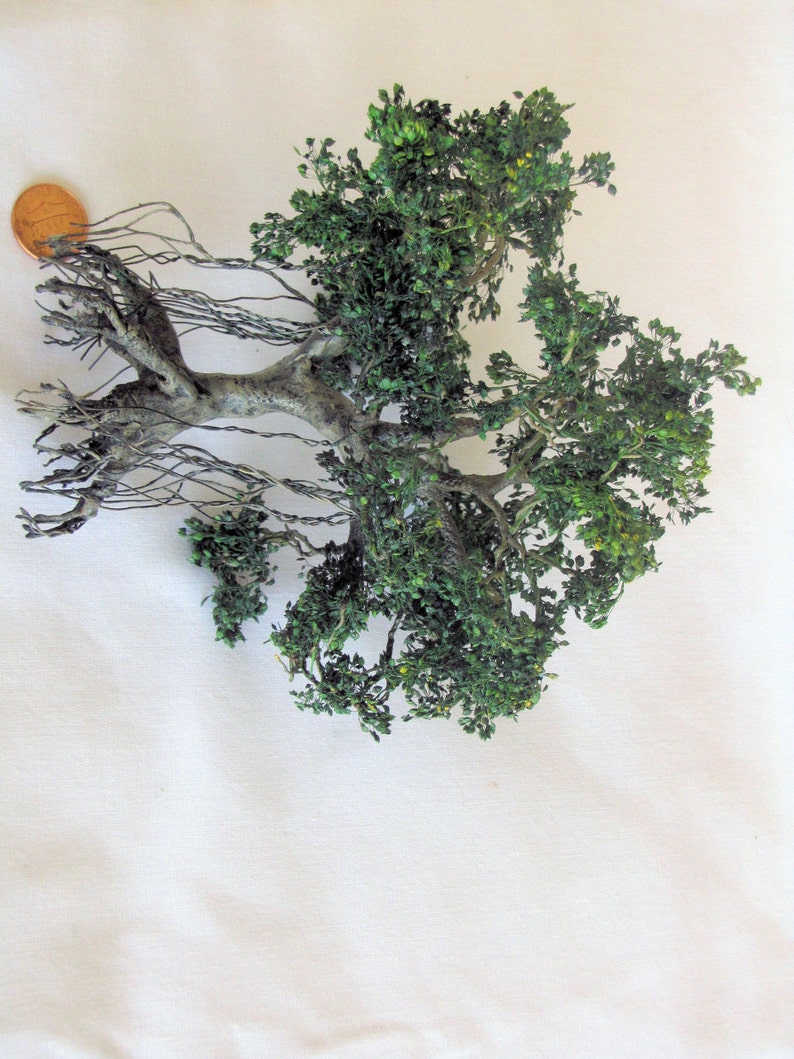 Puede incluir: Un modelo en miniatura de un &aacute;rbol con hojas verdes y ra&iacute;ces marrones. El &aacute;rbol est&aacute; hecho de un material que parece madera y tiene un aspecto realista.