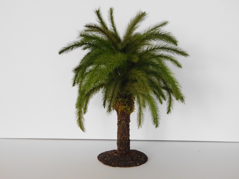 May include: A small, green, artificial palm tree with a brown, textured trunk and a base. The tree is on a white background.